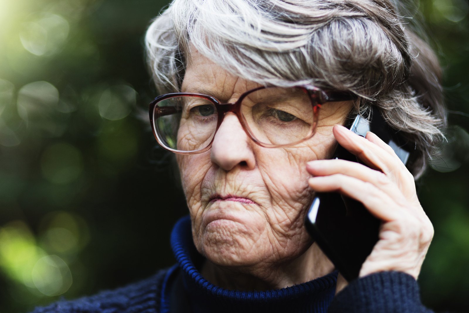 Eine wütend dreinschauende Seniorin am Telefon.