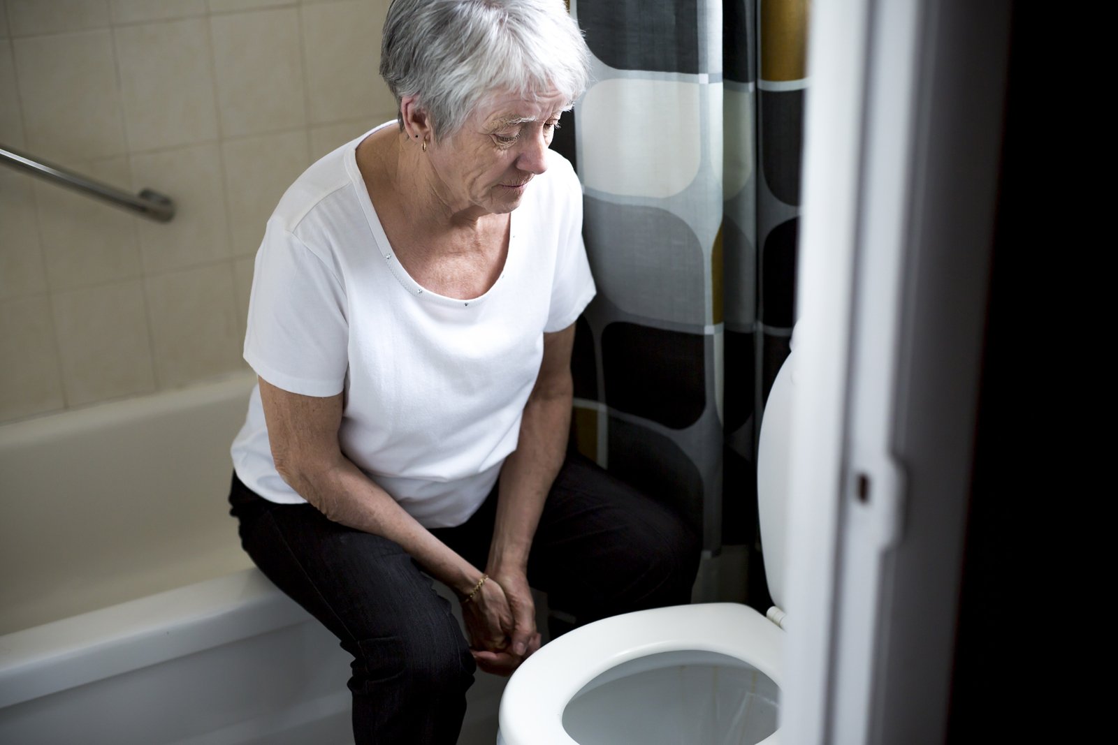 Eine Seniorin sitzt auf dem Badewannenrand. 