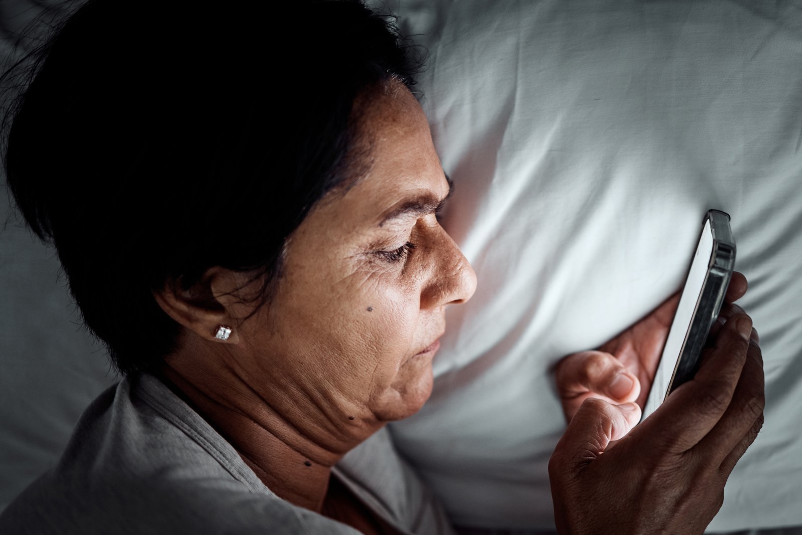 Eine Seniorin blickt im Bett aufs Handy.