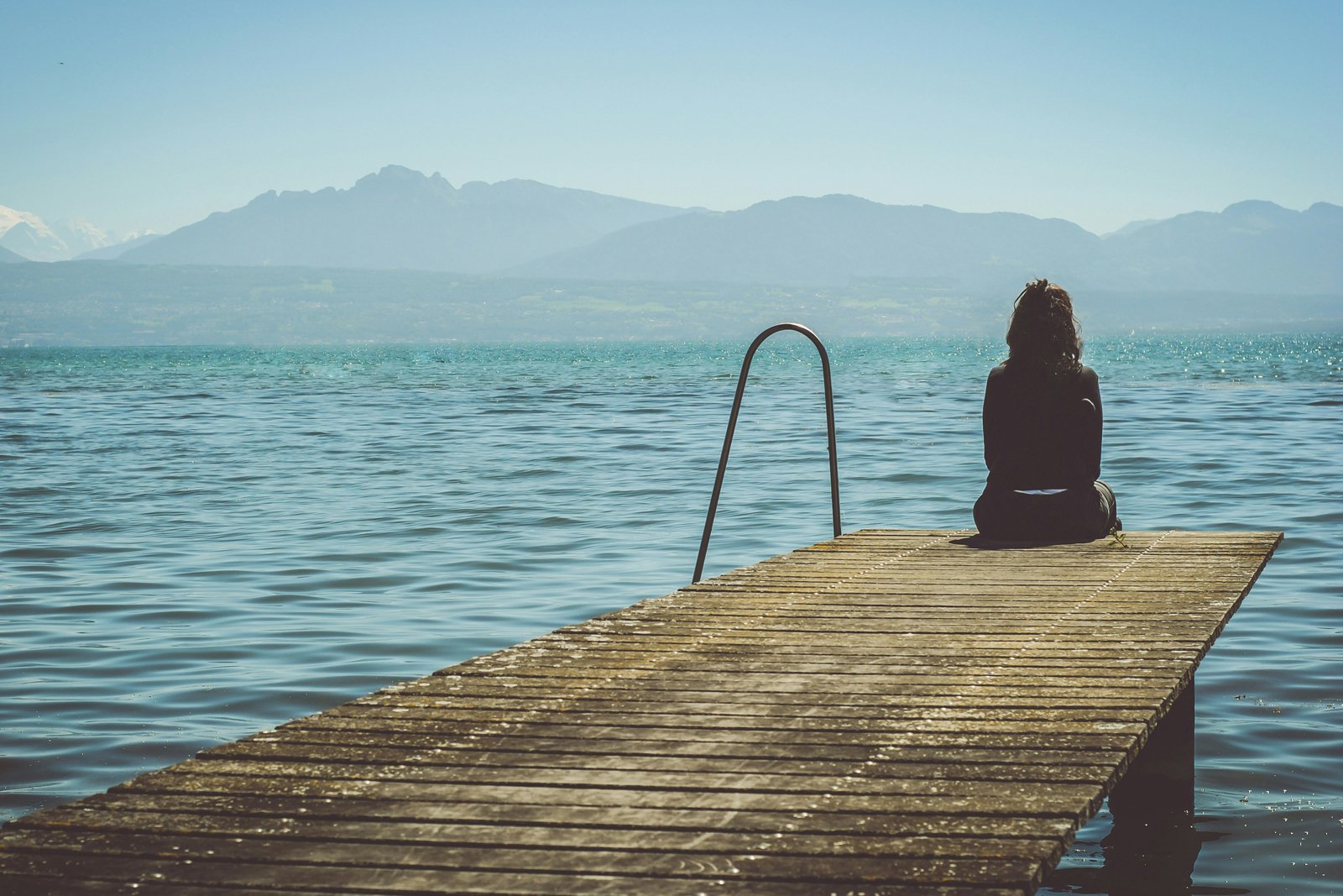 Eine Frau sitzt auf eine Bootssteg und blickt auf den See. 