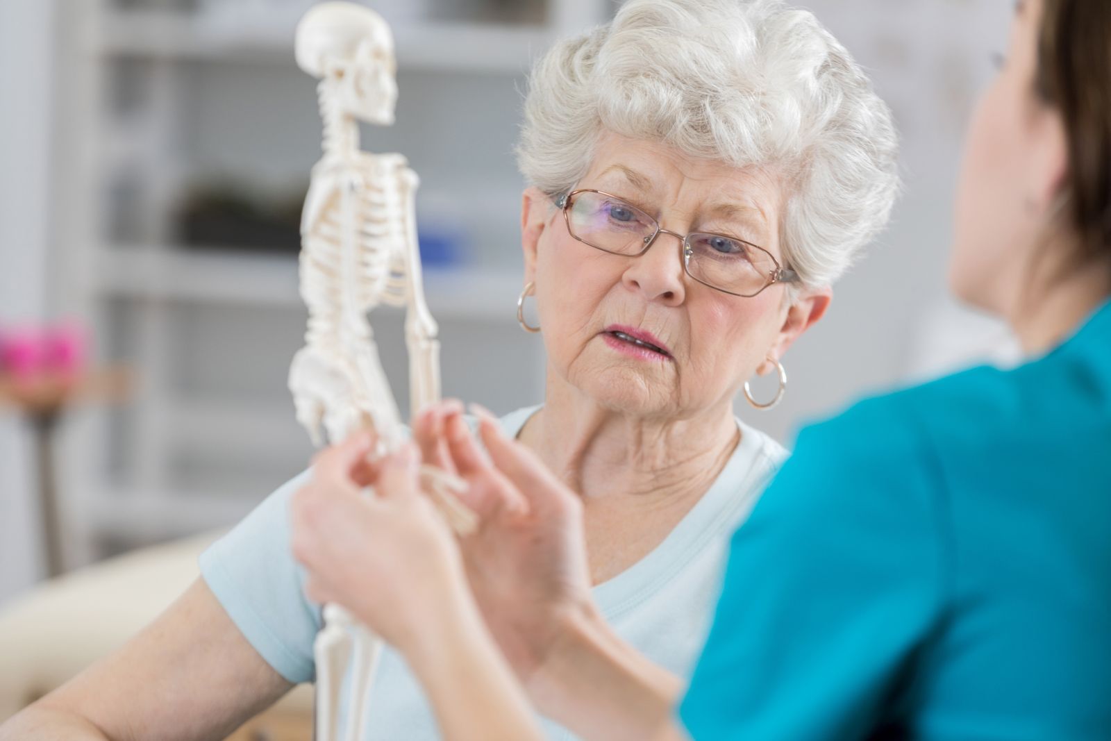 Eine Ärztin erklärt einer Patientin Osteoporose an einem Skelettmodell.