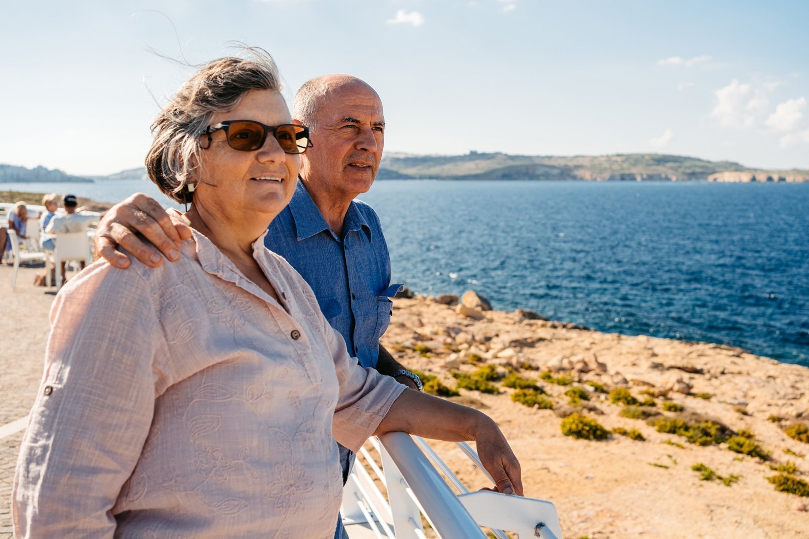 Ein Seniorenpaar blickt glücklich aufs Meer. 