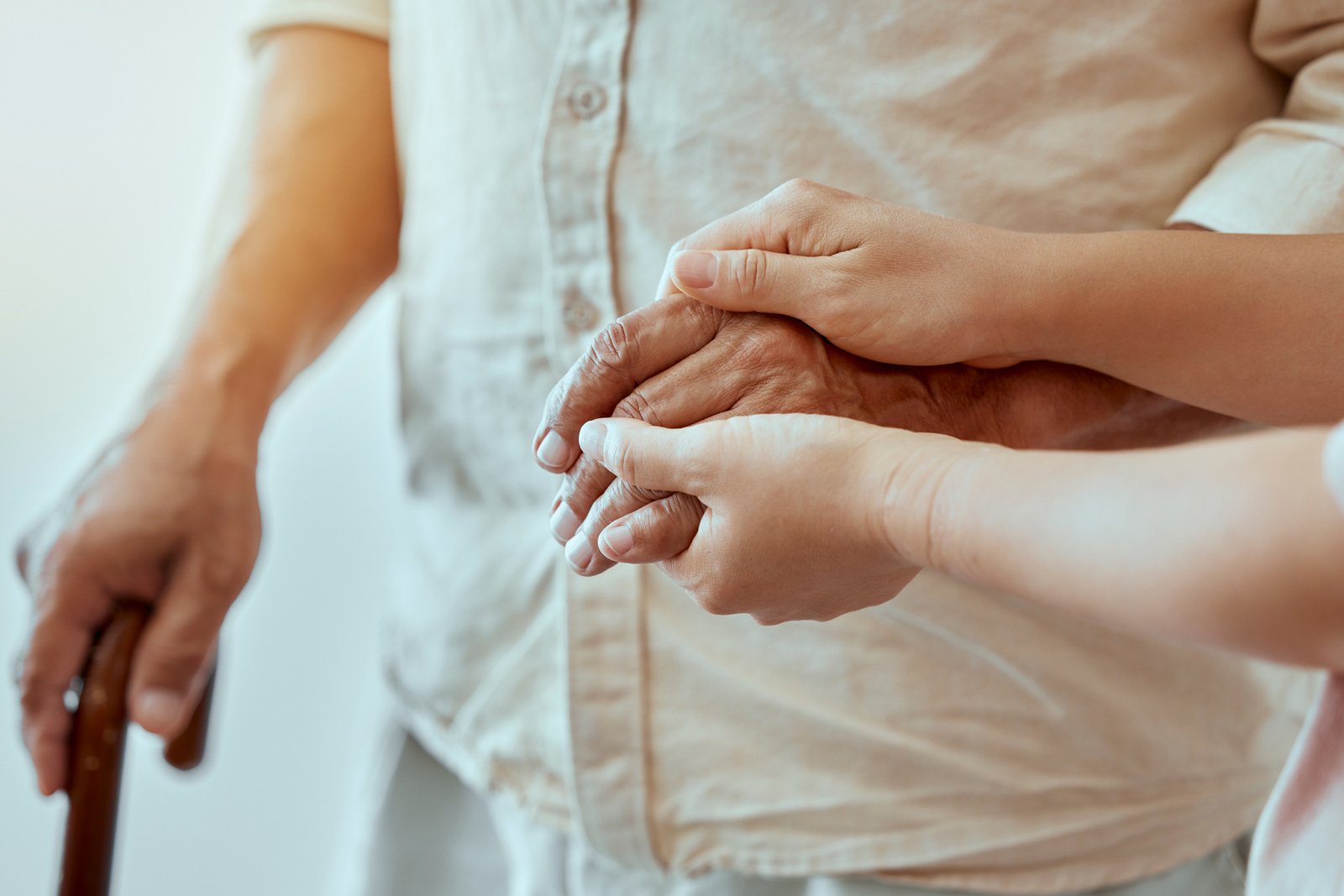 Eine helfende Hand hält die Hände eines Seniors. 