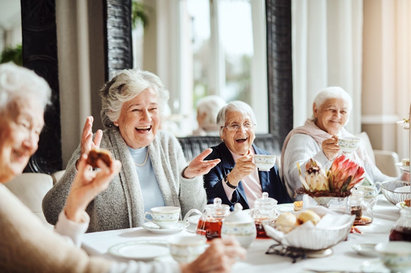 Eine Gruppe Seniorinnen sitzt am Tisch und lacht. 