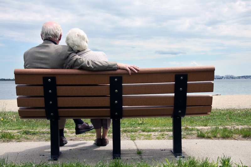 Ein älteres Paar sitzt auf einer Bank und blickt auf den See. 