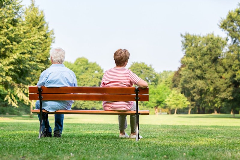 Ein älteres Ehepaar sitzt auf einer Parkbank. 