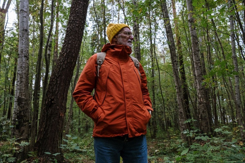 Ein Senior steht mitten im Wald. 